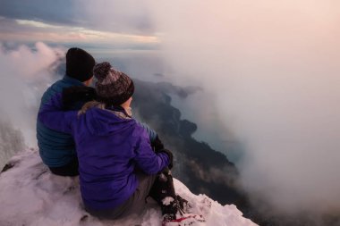 Sırasında canlı bir gün batımı manzarasına bakan sarp bir uçurum kenarında oturan genç bir çift. Üstünde tepe-in St Mark's Peak, Kuzey Vancouver, Bc, Kanada alınan.