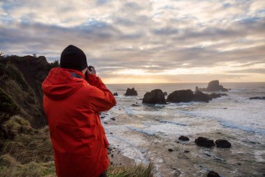 Bir kamera ile adam içinde belgili tanımlık geçmiş sağlam kayalık oluşumu ile güzel bir Pasifik Okyanusu sahilinde arıyor. Ecola State Park, deniz, savaş topu Beach, Oregon, ABD alınan.
