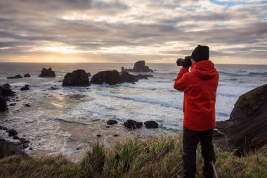 Bir kamera ile adam içinde belgili tanımlık geçmiş sağlam kayalık oluşumu ile güzel bir Pasifik Okyanusu sahilinde arıyor. Ecola State Park, deniz, savaş topu Beach, Oregon, ABD alınan.