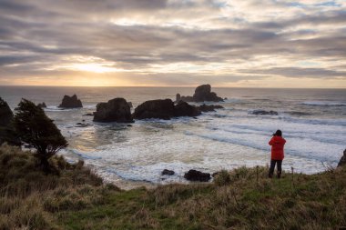 Bir kamera ile adam içinde belgili tanımlık geçmiş sağlam kayalık oluşumu ile güzel bir Pasifik Okyanusu sahilinde arıyor. Ecola State Park, deniz, savaş topu Beach, Oregon, ABD alınan.