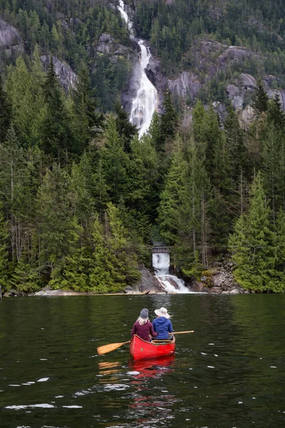 Couple adventurous people on a canoe are enjoying the beautiful waterfall, Shannon Falls. Taken in Squamish, North of Vancouver, BC, Canada.