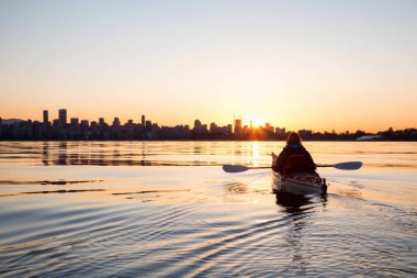 Deniz kanosundaki maceraperest kız, güneş doğarken kano yapıyor. Vancouver, British Columbia, Kanada 'da çekildi..
