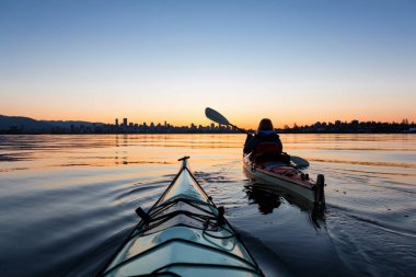 Arka planda şehir manzarası ile maceracı kız Deniz kanosu canlı kış gün doğumu sırasında. Şehir merkezinde alınan Vancouver, British Columbia, Kanada.