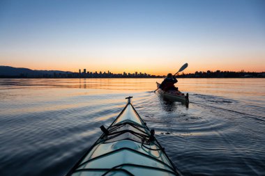 Arka planda şehir manzarası ile maceracı kız Deniz kanosu canlı kış gün doğumu sırasında. Şehir merkezinde alınan Vancouver, British Columbia, Kanada.