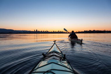 Arka planda şehir manzarası ile maceracı kız Deniz kanosu canlı kış gün doğumu sırasında. Şehir merkezinde alınan Vancouver, British Columbia, Kanada.