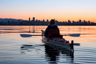 Arka planda şehir manzarası ile maceracı kız Deniz kanosu canlı kış gün doğumu sırasında. Şehir merkezinde alınan Vancouver, British Columbia, Kanada.