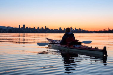 Arka planda şehir manzarası ile maceracı kız Deniz kanosu canlı kış gün doğumu sırasında. Şehir merkezinde alınan Vancouver, British Columbia, Kanada.