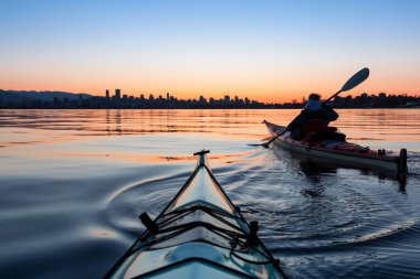Arka planda şehir manzarası ile maceracı kız Deniz kanosu canlı kış gün doğumu sırasında. Şehir merkezinde alınan Vancouver, British Columbia, Kanada.