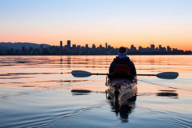 Arka planda şehir manzarası ile maceracı kız Deniz kanosu canlı kış gün doğumu sırasında. Şehir merkezinde alınan Vancouver, British Columbia, Kanada.