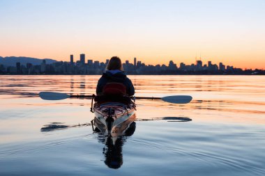 Arka planda şehir manzarası ile maceracı kız Deniz kanosu canlı kış gün doğumu sırasında. Şehir merkezinde alınan Vancouver, British Columbia, Kanada.