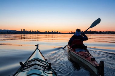 Arka planda şehir manzarası ile maceracı kız Deniz kanosu canlı kış gün doğumu sırasında. Şehir merkezinde alınan Vancouver, British Columbia, Kanada.