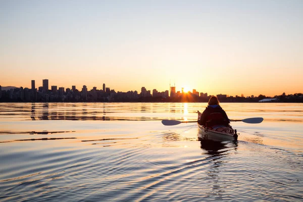 Adventurous girl on a sea kayak is kayaking during a vibrant sunny sunrise. Taken in Downtown Vancouver, British Columbia, Canada.