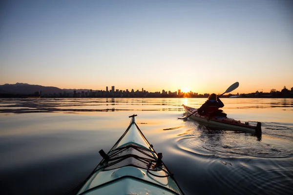 Adventurous girl on a sea kayak is kayaking during a vibrant sunny sunrise. Taken in Downtown Vancouver, British Columbia, Canada.