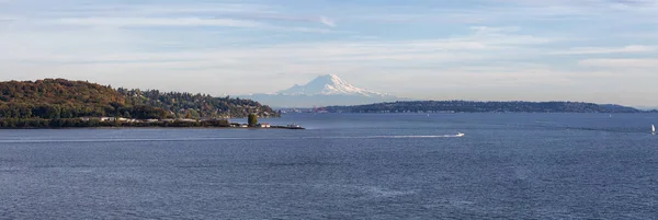 Beautiful View of Discovery Park and Mt Rainier in background on the Ocean Shore during a cloudy autumn evening. Taken in Smith Cove Park, Seattle, Washington, United States.