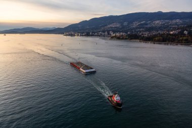 West Vancouver, British Columbia, Kanada. Pasifik Okyanusu kıyısındaki modern bir şehirde sonbahar güneşli ve bulutlu günbatımında römorkör görüntüsü.