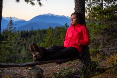 Maceracı Kız, güneşli bir sonbahar günbatımında dağlarda bir bankta dinleniyor. Götürülmüş Squamish, Vancouver 'ın kuzeyi, British Columbia, Kanada. Konsept: Macera, özgürlük, yaşam tarzı