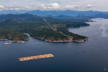 Puslu bir yaz günü, arka planda dağ manzarası olan keresteyi okyanusa çeken römorkör görüntüsü. Günışığı Sahili, Bc, Kanada.