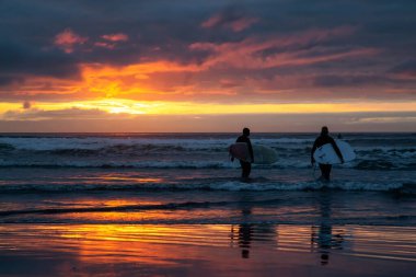 Dramatik bir yaz günbatımında kumlu sahilde okyanusa doğru yürüyen sörfçüler. Seaside, Oregon, Amerika Birleşik Devletleri 'nde çekildi..
