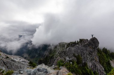 Bulutlu bir yaz sabahı engebeli bir kayalık dağın tepesinde duran maceraperest adam. Crown Dağı, Kuzey Vancouver, Bc, Kanada.