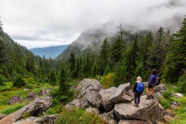 Maceracı Kız bulutlu bir yaz sabahı dağlarda güzel yeşil ormanlarda yürüyüş yapıyor. Crown Dağı, Kuzey Vancouver, Bc, Kanada.
