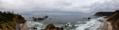 Ecola State Park, Cannon Beach, Oregon, ABD. Pasifik Okyanusu kıyısındaki Sandy ve Rocky Sahili 'nin güzel Panoramik Manzarası bulutlu bir yaz gündoğumu sırasında.