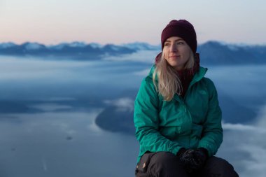 Vancouver, Bc, Kanada - 25 Kasım 2019: Renkli kış günbatımında kar kaplı dağın tepesinde oturan maceracı sarışın beyaz kız.