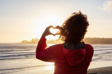 Long Beach, Near Tofino ve Ucluelet Vancouver Adası, Bc, Kanada. Maceraperest Kız, arka planda Pasifik Okyanusu kıyısında altın gün batımlı elleri ile Hearth Şekli 'ni yapıyor..