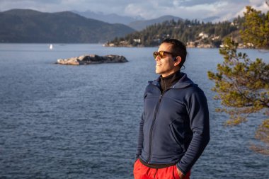 Bulutlu ve güneşli bir günbatımında, doğada, Maceracı bir Latin adamın portresi. Deniz Feneri Parkı, At Nalı Koyu, Batı Vancouver, Bc, Kanada.