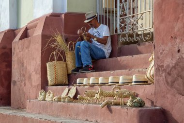Trinidad, Cuba - June 12, 2019: Cuban Man making art in the streets near Plaza Mayor during a colorful sunny evening. clipart