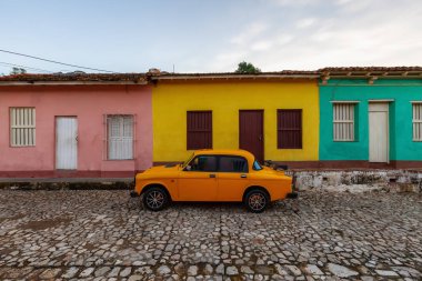 Güneşli bir gündoğumu sırasında arka planda kilisesi olan küçük bir Küba kasabasının sokaklarında eski klasik bir taksi manzarası. Trinidad, Küba.