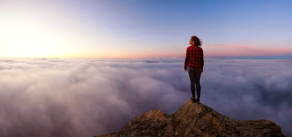 Chica aventurera en una montaña rocosa por encima de las nubes — Foto de Stock