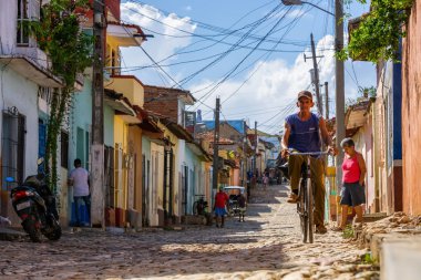 Trinidad, Küba - 11 Haziran 2019: Canlı güneşli bir günde Küba 'nın eski bir kasabasında bisiklet süren Kübalı insanlar.