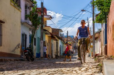 Trinidad, Cuba - June 11, 2019:  Cuban people riding a bicycle on an Old Street of a small Cuban Town during a vibrant sunny day. clipart