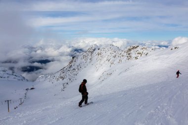 Güneşli ve bulutlu bir kış gününde karlı bir dağın tepesinde snowboard yapan adam. Blackcomb Dağı, Whistler, British Columbia, Kanada.