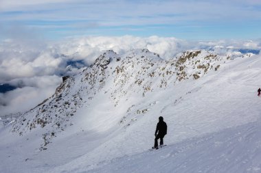 Güneşli ve bulutlu bir kış gününde karlı bir dağın tepesinde snowboard yapan adam. Blackcomb Dağı, Whistler, British Columbia, Kanada.