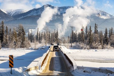 Golden, British Columbia, Kanada. Dar Köprü donmuş nehrin üzerinden geçiyor. Arka planda endüstrilerin dumanı var..