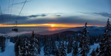 Seymour Dağı, Kuzey Vancouver, British Columbia, Kanada. Güneşli ve bulutlu bir kış günbatımında bir kayak merkezinin tepesine çıkarken panoramik manzara.