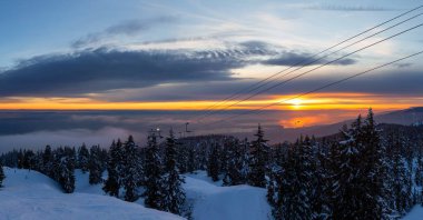 Seymour Dağı, Kuzey Vancouver, British Columbia, Kanada. Güneşli ve bulutlu bir kış günbatımında bir kayak merkezinin tepesine çıkarken panoramik manzara.