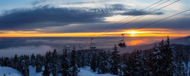 Seymour Dağı, Kuzey Vancouver, British Columbia, Kanada. Güneşli ve bulutlu bir kış günbatımında bir kayak merkezinin tepesine çıkarken panoramik manzara.
