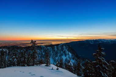 Renkli ve canlı kış günbatımında arka planda şehirle birlikte Kanada Doğa Alanı taze beyaz karla kaplıydı. Seymour Dağı, Kuzey Vancouver, British Columbia, Kanada.