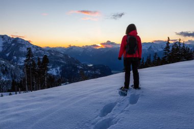 Canlı ve renkli kış günbatımında bir dağın tepesinde kar ayakkabısı giyen maceraperest kız. Anif Tepesi, Squamish, British Columbia, Kanada 'da çekildi. Kavram: Keşif, macera