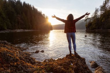 Kanada 'da canlı kış günbatımında elleri havada maceraperest bir kız. Vancouver, British Columbia, Kanada 'daki Jug Island Trail' de yürüyüş. Kavram: Özgürlük, Keşif, Sağlık