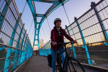 Güneşli bir gün batımında, Otoyol üzerindeki yaya köprüsünde bisiklete binen beyaz kadın. Surrey, Vancouver, British Columbia, Kanada 'da çekilmiş. Alternatif Taşımacılık