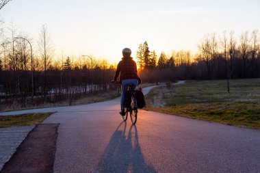 Güneşli bir günbatımında yaya yolunda bisiklete binen beyaz bir kadın. Surrey, Vancouver, British Columbia, Kanada 'da çekildi.