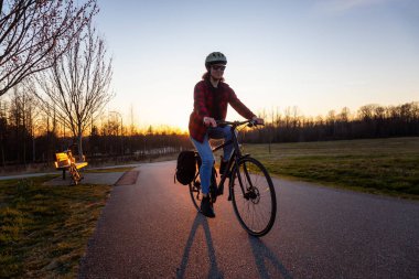 Güneşli bir günbatımında yaya yolunda bisiklete binen beyaz bir kadın. Surrey, Vancouver, British Columbia, Kanada 'da çekildi.