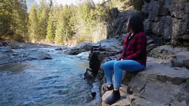 Девушка, сидящая у реки в Канадском горном пейзаже — стоковое видео
