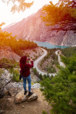 Adventurous Girl Taking Pictures of a Scenic Road in the Canadian Mountain Landscape clipart