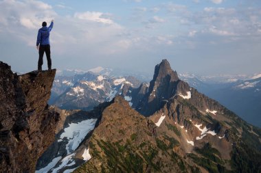 Dik bir kayalığın üstünde elleri havada maceraperest bir yürüyüşçü..