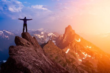 Dik bir kayalığın üstünde elleri havada maceraperest bir yürüyüşçü..