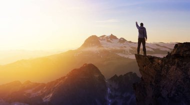 Dik bir kayalığın üstünde elleri havada maceraperest bir yürüyüşçü..